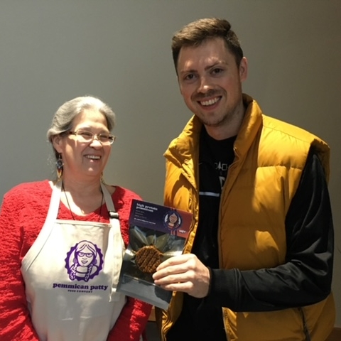 Patt with an unidentified individual at the Turtle Mountain Heritage Center in Belcourt holding the hand-pressed original version of pemmican patties